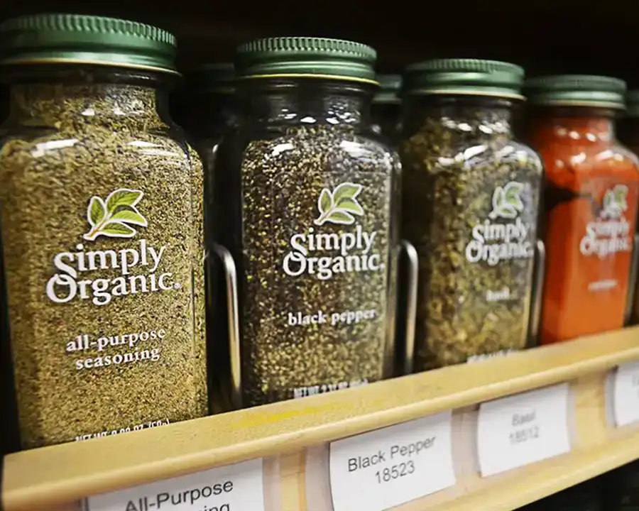 Close-up of organic seasoning jars with green lids, including black pepper and basil, on a shelf at Food Fantasies near Jacksonville, IL
