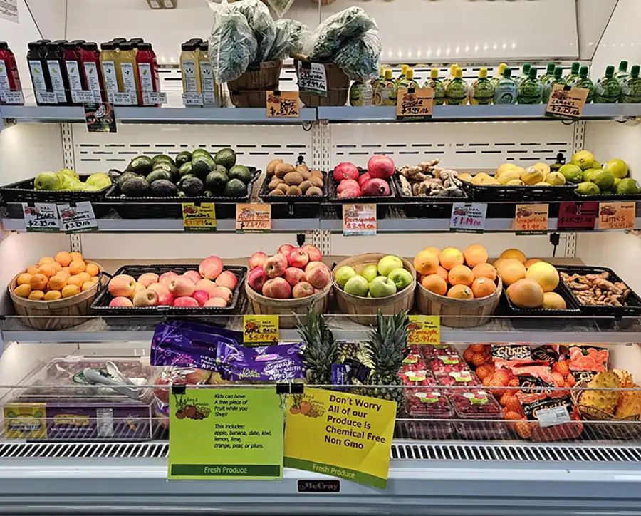 Refrigerated produce display with apples, oranges, grapefruit, pineapples, and fresh ginger at Food Fantasies near Jacksonville, IL