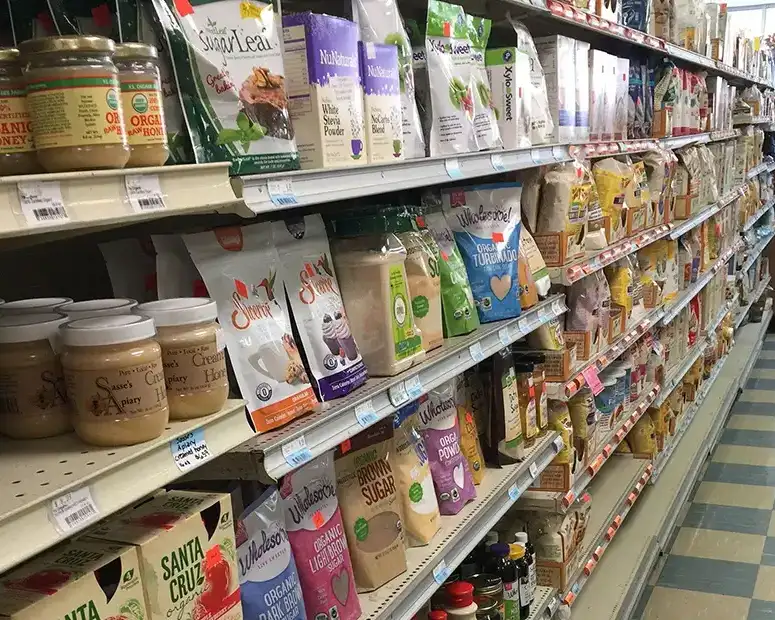 Shelves of baking sweeteners, brown sugar, stevia, snacks, and local honey beside a checkered floor at Food Fantasies near Jacksonville, IL