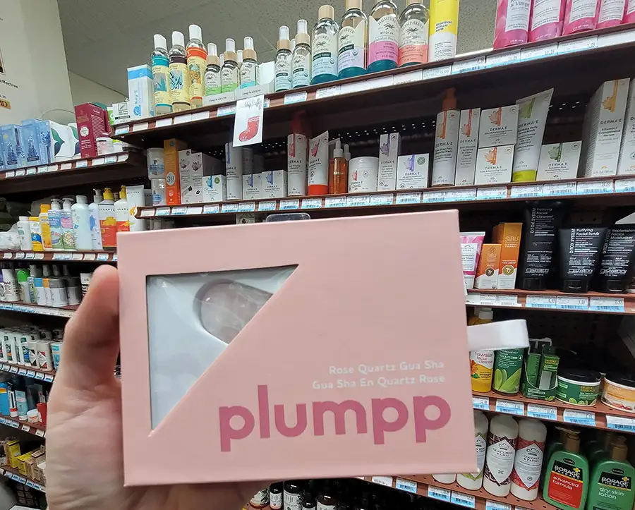 Customer holding a pink rose quartz gua sha box beside shelves of natural face and body care at Food Fantasies near Jacksonville, IL