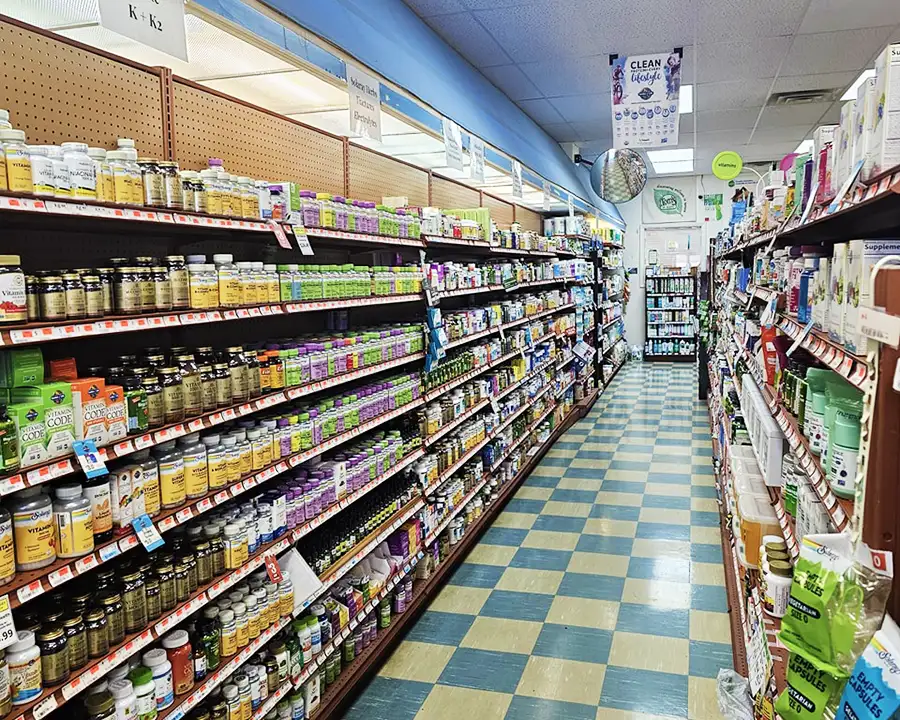 Shelves stocked with vitamins, minerals, and natural supplements along a blue and yellow tiled aisle at Food Fantasies near Sherman, IL